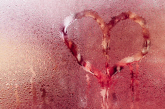 Romantic heart painted on fogged up window, water droplets distorting view. Tender yet mysterious gesture left for someone special. red romantic background