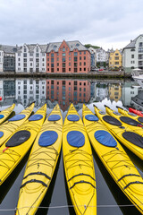 Bright yellow kayaks moored on the calm waters of Brosundet canal in Alesund, Norway, with colorful Art Nouveau buildings reflected in the background on a cloudy day