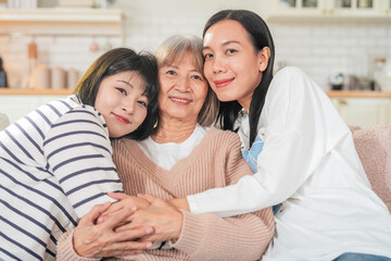 senior woman, her daughter and her granddaughter sitting on the sofa at home Asian family lifestyle...