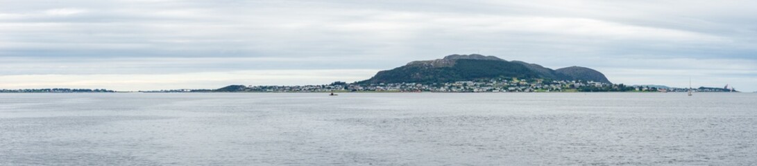 Cloudy day over Giske island near Ålesund, Norway, featuring green meadows, calm sea, and rugged coastline under a soft, diffused light on the western fjords