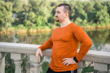 A man in workout clothes rests on a railing with a scenic view