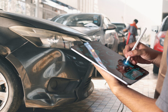 Technician evaluates vehicle damage using a digital tablet at an auto repair shop, likely for insurance or repair documentation. - Powered by Adobe