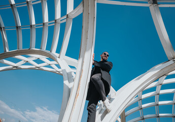 Stylish man confidently climbing a contemporary structure under a bright blue sky.