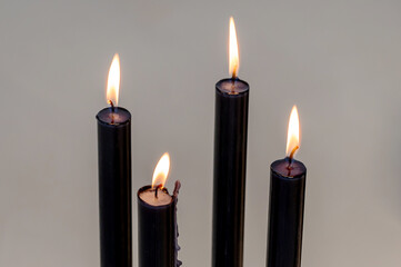 Four burning black candles illuminating a neutral background