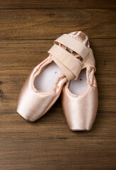 Pink ballet pointe shoes resting on wooden floor