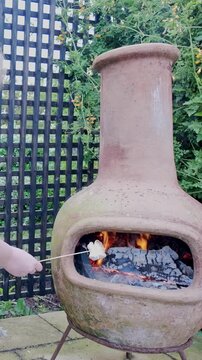 Toasting marshmallows over chiminea barbecue fire by hand VERTICAL shot