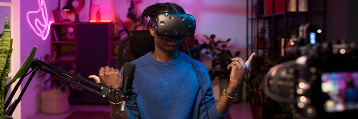 Man engaged in virtual reality experience while communicating in modern studio with illuminated neon lights. Immersed in scene, expressing gesture with hands