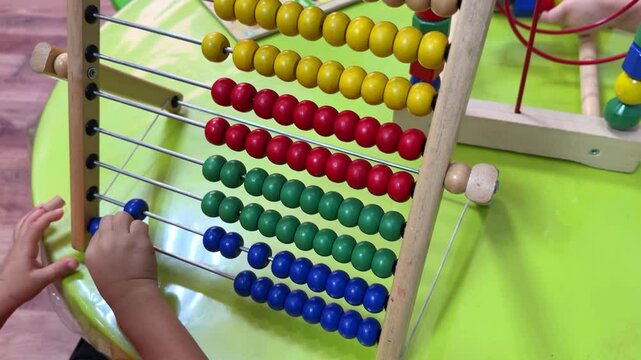 A young child interacts with a colorful abacus, learning to count and sort. Perfect for educational content, e-learning visuals, or preschool promos. Captured in crisp 4K resolution.