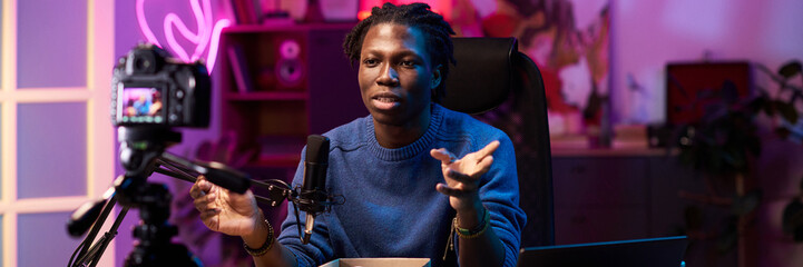 Portrait of passionate Black person sitting in front of camera, recording engaging content in a...