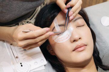 Fototapeta premium Young southeast asian woman finds peace during beauty salon procedure applying eyelash extension. Meticulous work enhances eyelashes eyes beauty through cosmetic extension promoting health