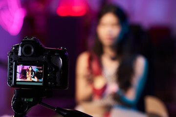 Asian woman recording promotional video content using professional camera in studio with blurred background, ensuring high-quality production for viewers using advanced equipment