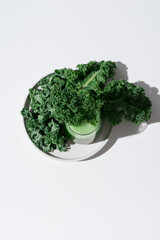 Jugo de col rizada verde y hojas frescas de col rizada en un plato sobre fondo blanco