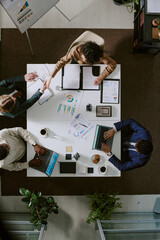 Four professionals sitting at office table, discussing work using laptops and documents. Top down view provides perspective of collaborative workspace © AnnaStills