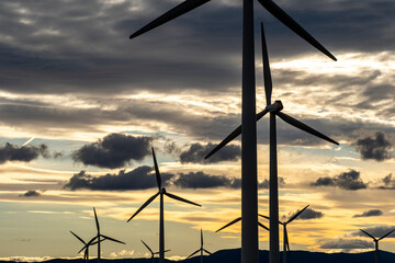 Close-up of wind turbines against golden clouds and blue sky in Zaragoza, Spain, ideal for green energy, sustainability, and renewable energy industry stock visuals.