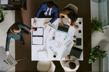 Group of professionals collaborating around table, reviewing documents and charts, discussing...