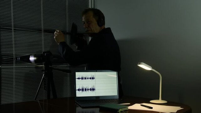 Spy concept: a man with headphones records audio through a window, watching from an office.