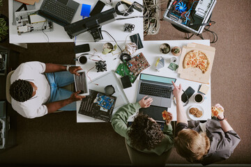Group of people discussing at cluttered workspace with various electronic devices. Team members...