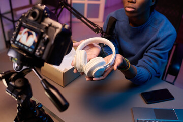 Person holding white headphones while engaging audience during livestream broadcast with camera and...