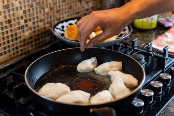 The hand of a man placing molded pies on a frying pan with butter.
