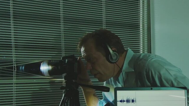 Surveillance and wiretapping: an agent in a suit records sounds and video from outside through a window with blinds