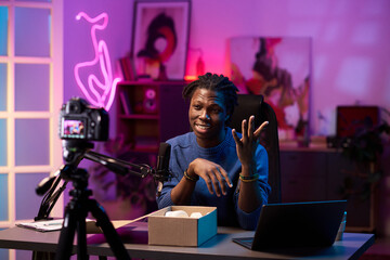 Content creator filming in modern, artistically lit studio with laptop. Engaging hand gesture while...
