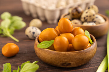Pile of smoked quail eggs in bowl on a brown wooden. side view, selective focus.