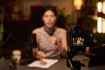 Woman speaking into microphone while camera captures video content, suitable for educational or...