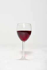 Elegant glass of red wine centered on white surface. Simple, minimalistic background enhances deep red hue, creating visual focus. Soft lighting adds sophistication