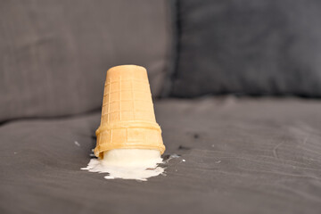Ice cream cone overturned on grey fabric couch, vanilla melting into upholstery. Soft lighting...