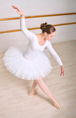 Young female ballerina with brown hair rehearses in white costume on wooden floor. Warm lighting enhances graceful movements and focuses on technique © TRAVELARIUM