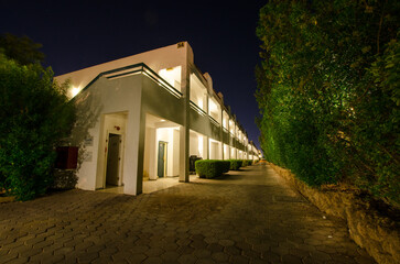 Modern hotel facade under night sky, featuring illuminated pathway and lush greenery. Subdued...