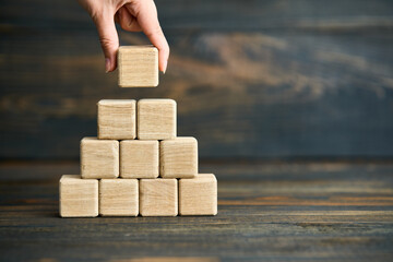 Hand placing last wooden cube on pyramid stack