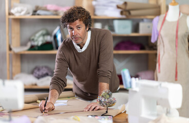 Adult male tailor drawing pattern on paper in sewing workshop