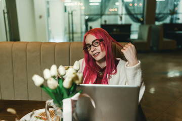 A woman with red hair is sitting with a laptop in a cafe