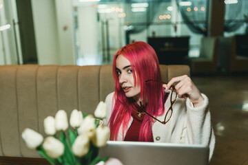 A woman with red hair is sitting with a laptop in a cafe