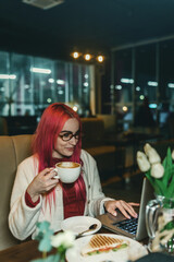 A woman with red hair is sitting with a laptop in a cafe