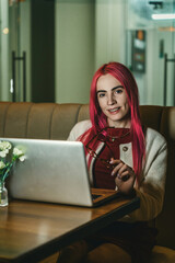 A woman with red hair is sitting with a laptop in a cafe