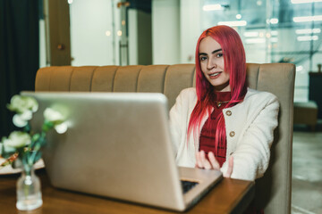 A woman with red hair is sitting with a laptop in a cafe
