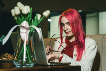 A woman with red hair is sitting with a laptop in a cafe