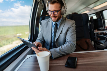 Young businessman wearing headphones and using digital tablet while traveling by train, enjoying music and staying productive during his commute