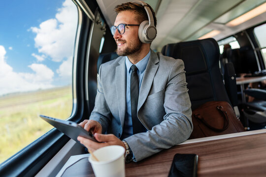 Young businessman wearing headphones and using digital tablet while traveling by train, enjoying music and staying productive during his commute - Powered by Adobe