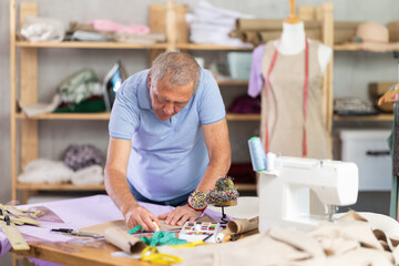 Elderly male tailor drawing pattern markings on fabric in sewing workshop