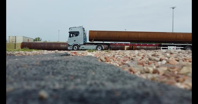 a truck makes a maneuver with a long trailer with a large steel pipe on top
