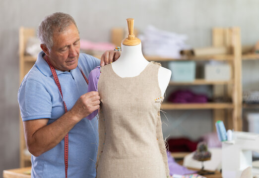 Elderly male tailor adjusting clothes on mannequin in sewing workshop - Powered by Adobe