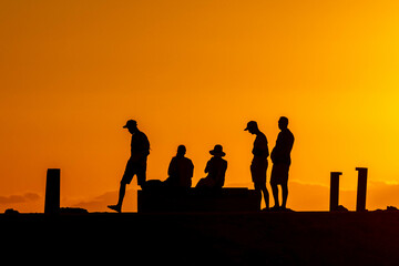 Silhouettes of people on a pier at sunset with glowing orange sky and sea horizon. Side, Turkey, Mediterranean region.