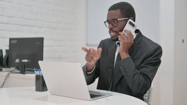 Professional African American businessman on an urgent phone call, focused at his laptop