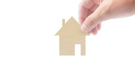 Hand placing paper house model on business concept minimalist environment close-up view