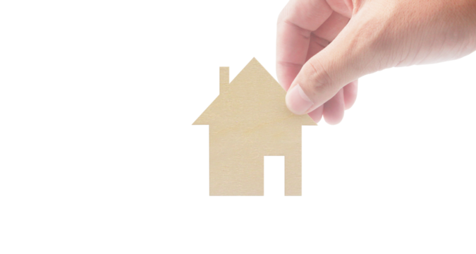 Hand placing paper house model on business concept minimalist environment close-up view