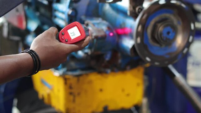 Close up technician hand holding a digital thermometer gun, and check temperature of the automatic transmission during the running test at test bench.