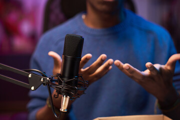 African American podcast host gesturing passionately while speaking into professional microphone setup. Capturing engaging moment with out-of-focus colorful background
